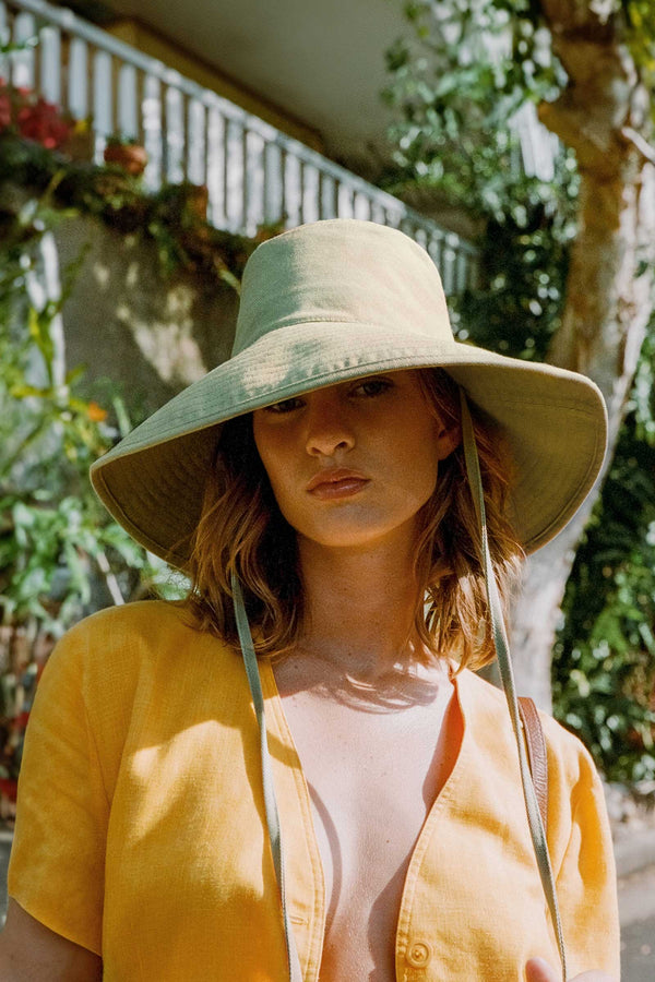 Model wearing a green cotton bucket hat outdoors with foliage in the background.