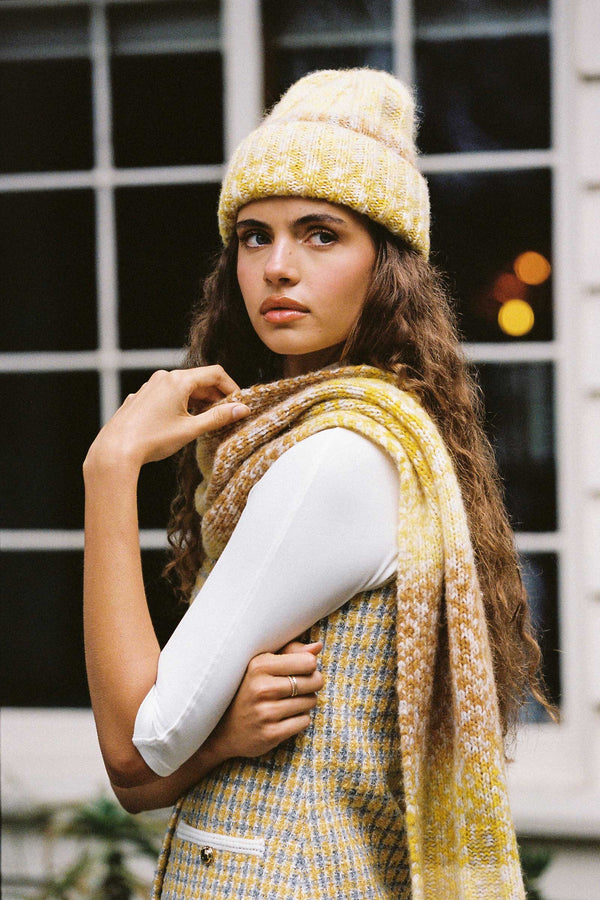 Model wearing a yellow and caramel ribbed scarf with a matching beanie, showcasing the texture and colors.