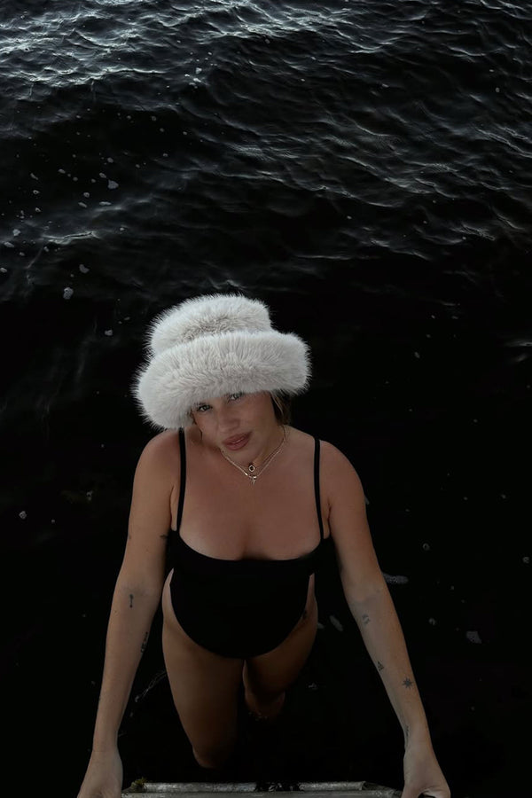 Model wearing Snuggle Bucket hat in faux fur, standing in water