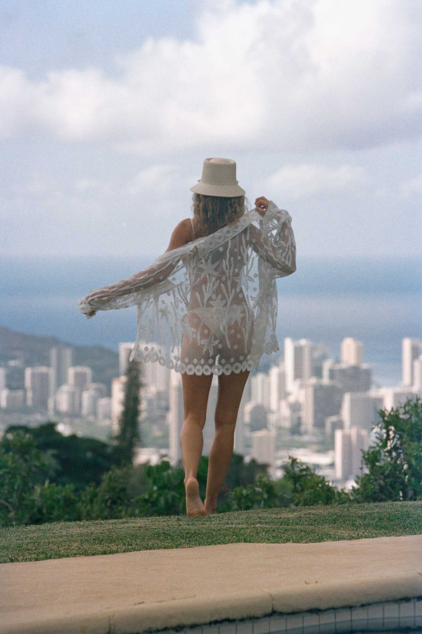 A woman wearing The Inca Bucket straw hat, standing by a pool with a city view.