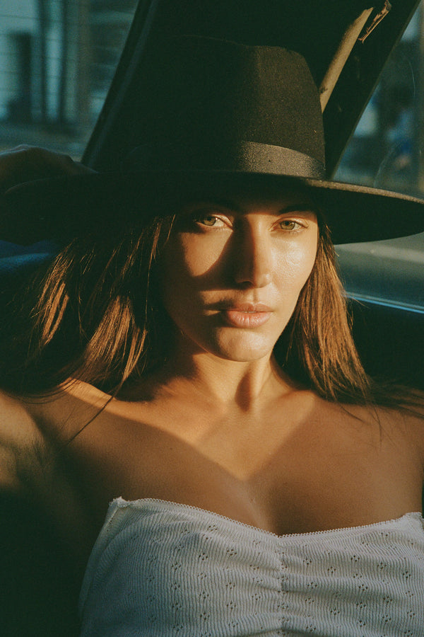 Model wearing a black wool fedora hat, the Noir Rancher, with natural lighting highlighting the features.