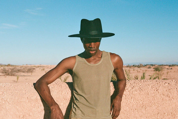 Model wearing a black wool fedora hat against a desert backdrop