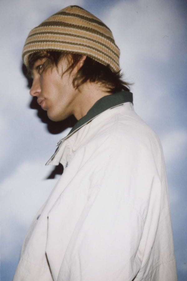 Profile view of a model wearing a brown striped Momo Beanie against a cloudy background.