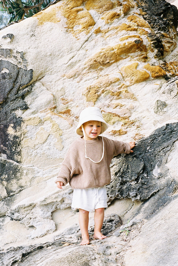 Child wearing a beige cotton bucket hat while climbing on rocks