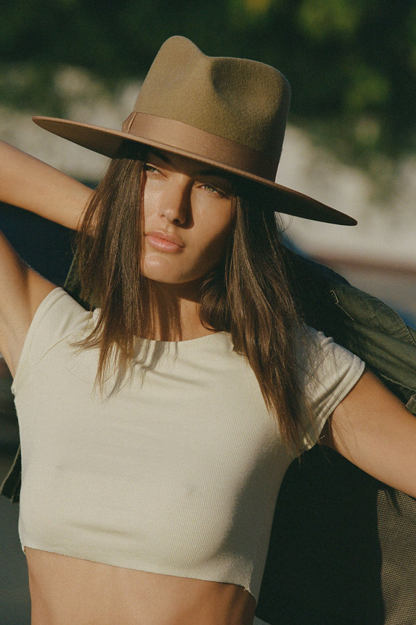 A model wearing a brown hat and a cropped top, posing outdoors.